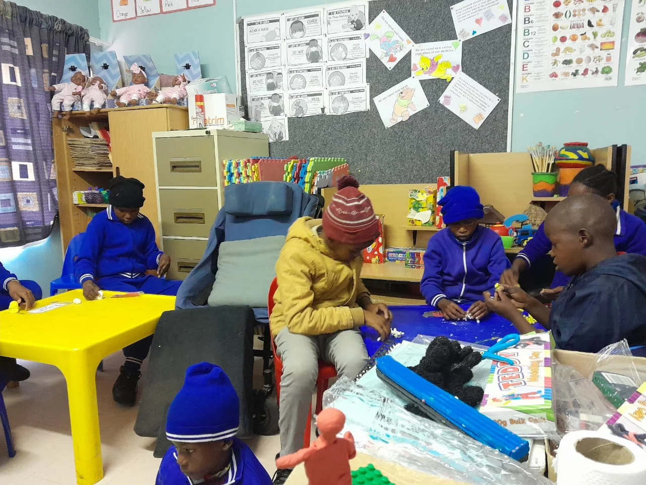 Children and staff working with learning materials around colourful classroom tables.